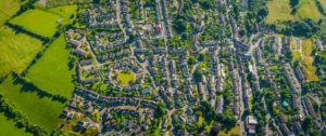 Aerial view over homes, streets and suburban community at the edge of a country town surrounded by green pasture and farmland, Stroud, UK.